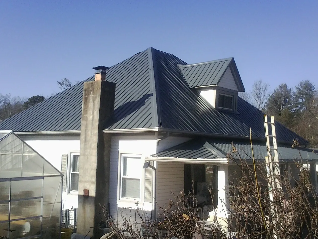 Dark blue standing seam metal roof on a white farmhouse with dormer — Slate & Tile Roof Repair by Roofing Brothers in Borup