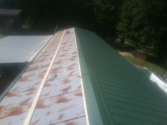 Old rusted panels beside newly installed green metal roofing — Wind Damage Roof Repair by Roofing Brothers in Borup