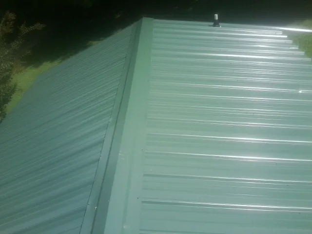 New green metal panels meeting at the ridge of a roof — Flat Roof Repair work by our crew in Borup