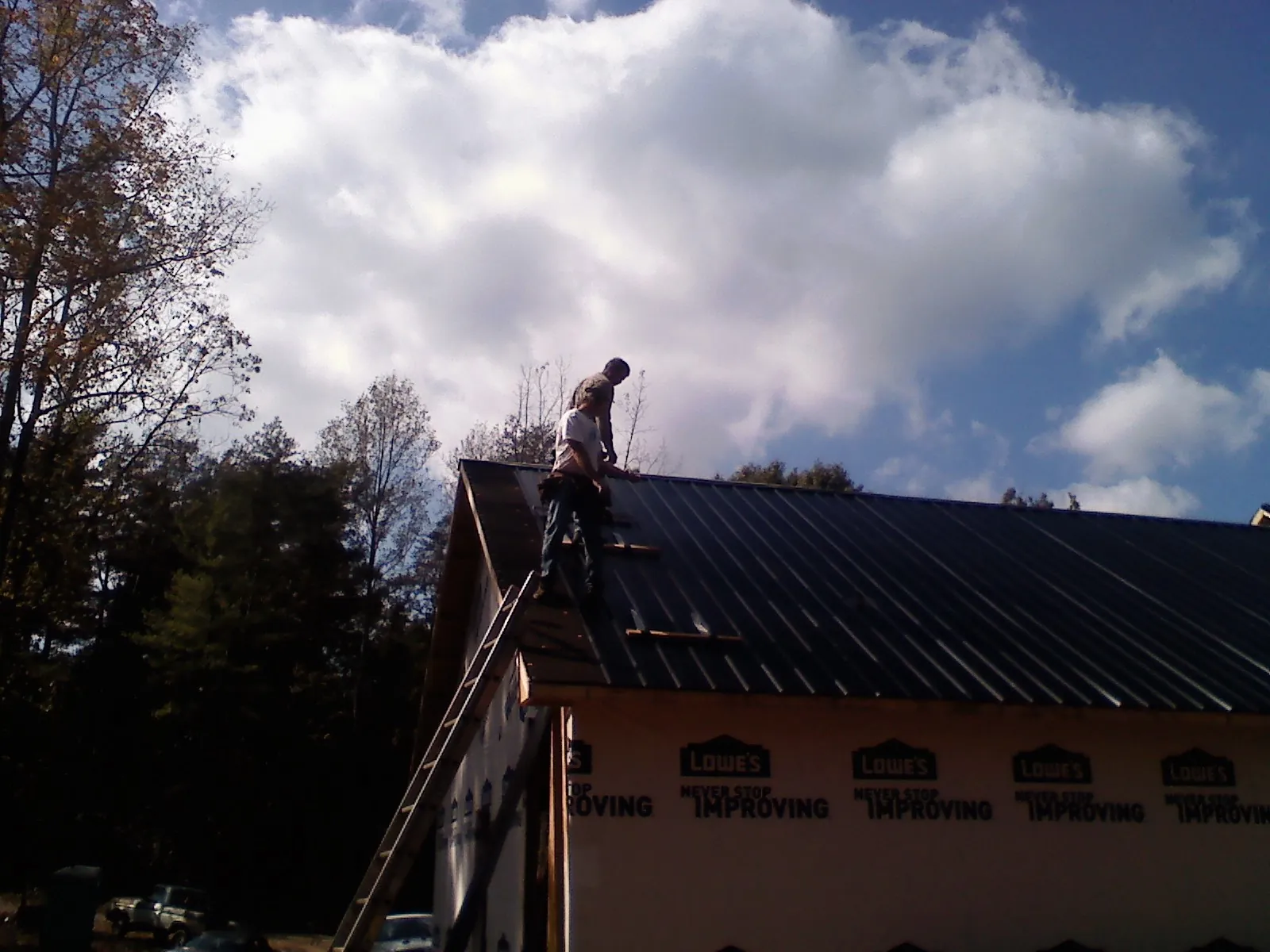 Roofer fastening dark metal panels high against a cloudy sky, from a Roof Inspection job in Borup