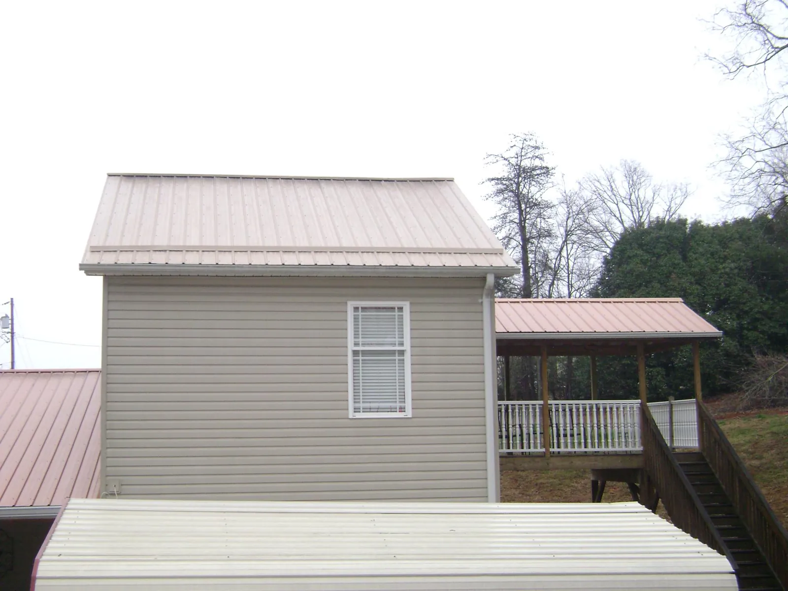 Tan metal roofs on a two story addition and attached porch, from a Roof Replacement job in Borup
